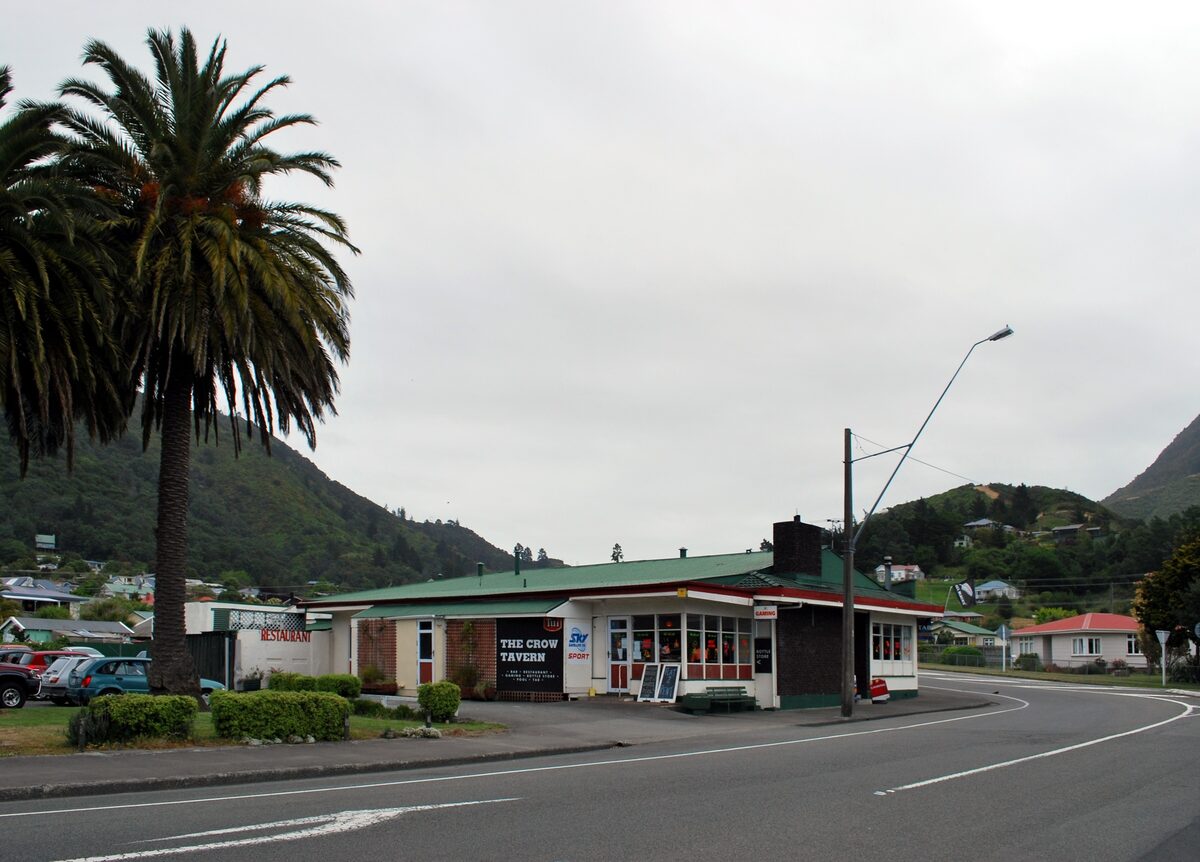Low green-roofed tavern building beside a road and a large palm tree, Picton