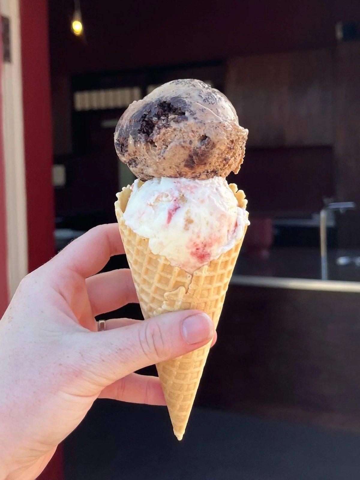 Two scoops of Only Scoop ice cream in a waffle cone, photographed in front of the shop counter.