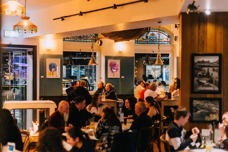 Warm dining room with occupied tables, stained-glass details, pendant lights and historic wall displays.