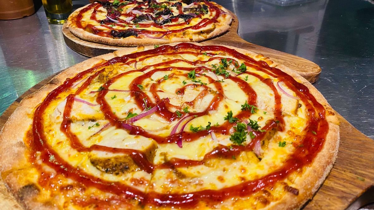 Two finished wood-fired pizzas on wooden serving boards in Scoozi's kitchen.