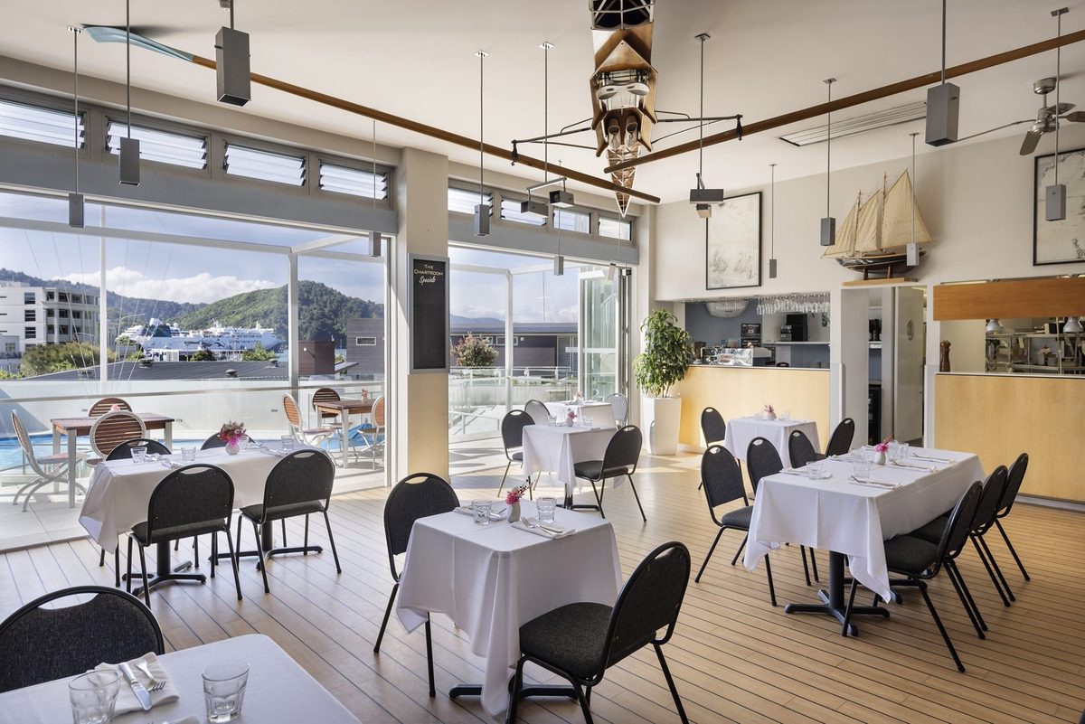 Bright nautical-themed Chartroom dining room with set tables, open kitchen and harbour outlook.