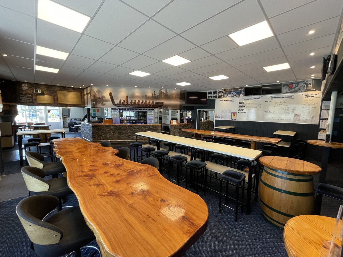 Main bar seating area with live-edge timber table, stools, barrel table, service bar and wall mural.
