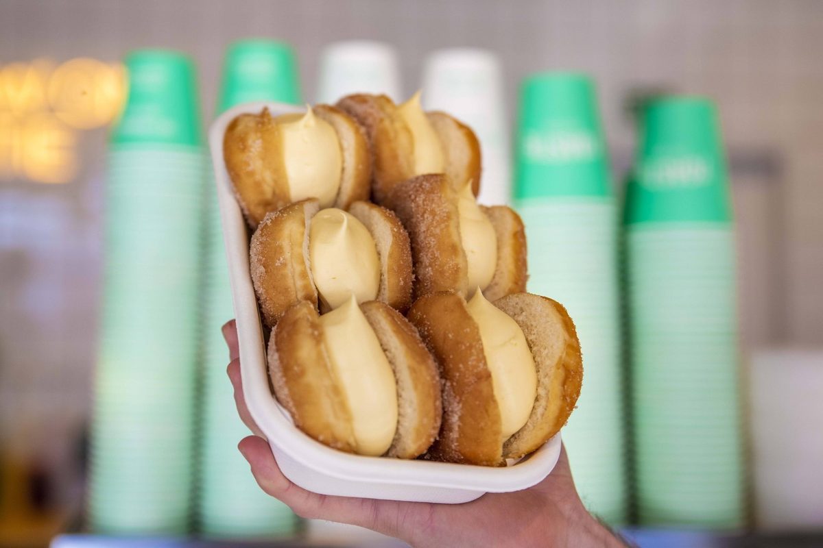 A tray piled with sugar-coated doughnuts filled generously with pale yellow cream.